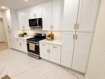Bright kitchen with white cabinets, a gas range and marble-look tile floors