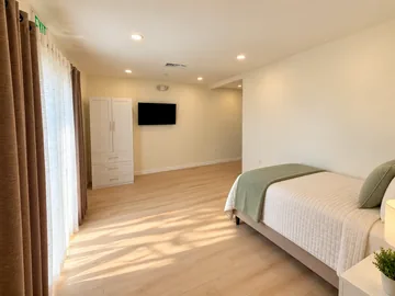 Bedroom with a made bed, wardrobe, wall TV and sunlit sheer curtains