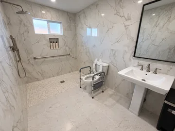 Walk-in shower with a grab bar, handheld shower head and toilet safety frame